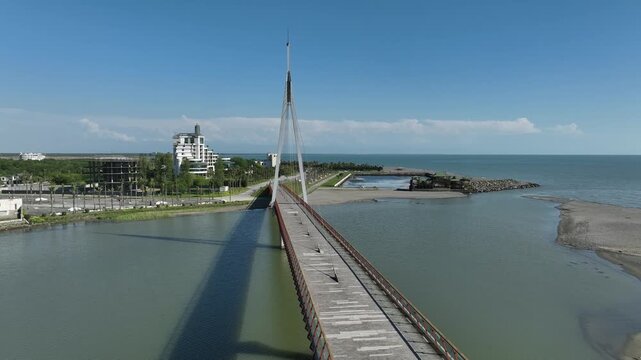 Aerial view of Anaklia resort in Georgia featuring the futuristic observation tower, pedestrian bridge over Enguri river, sandy beach, and Black Sea coastline on a sunny day.