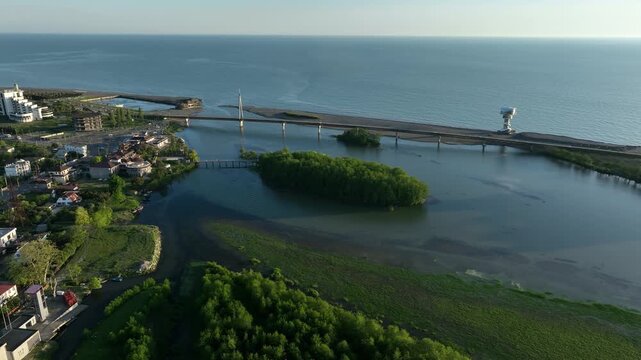 Aerial view of Anaklia resort in Georgia featuring the futuristic observation tower, pedestrian bridge over Enguri river, sandy beach, and Black Sea coastline on a sunny day.