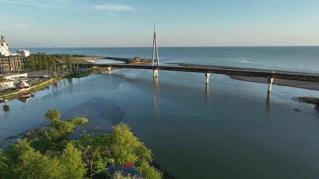Aerial view of Anaklia resort in Georgia featuring the futuristic observation tower, pedestrian bridge over Enguri river, sandy beach, and Black Sea coastline on a sunny day.