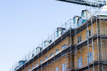Fototapeta premium Building under construction with scaffolding and cranes, showcasing a multi-story structure with windows and a clear blue sky in the background