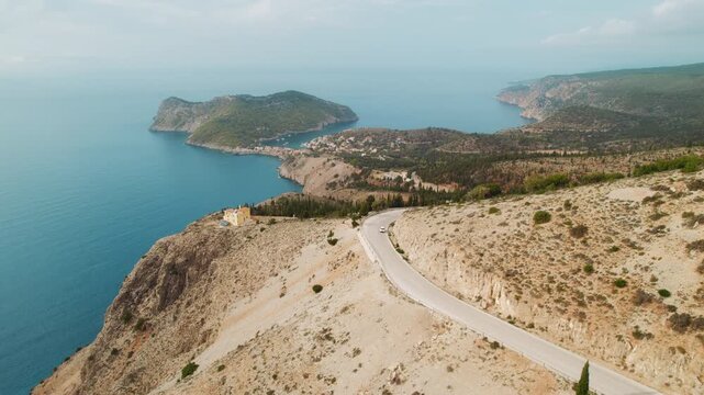Aerial view of a winding coastal road above a serene bay on Kefalonia during summer daylight