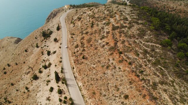 White car driving on lonely coastal road above the Ionian Sea in Kefalonia Greece