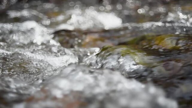 Rapids on shallow mountain stream making splatters, fast flow over uneven stone bottom and lovely bokeh in background