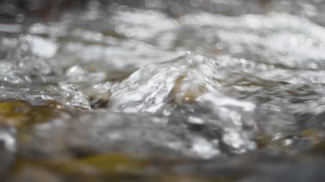 Rapids on shallow mountain stream making splatters, fast water flow over stone close up, lovely background
