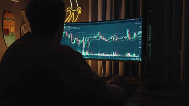 Professional trader or investor working at multiple monitors with stock market charts, financial data, and trading graphs.