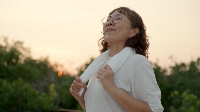 Active senior woman exercising and breathing fresh air in public park. Healthy aging, wellness, mobility, fitness and retirement lifestyle with clean outdoor environment concept.

