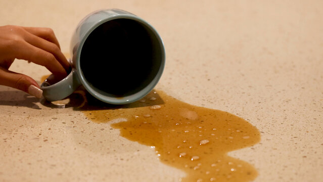 Hand Reaching for Tipped Over Coffee Mug with Liquid Spilled on Counter