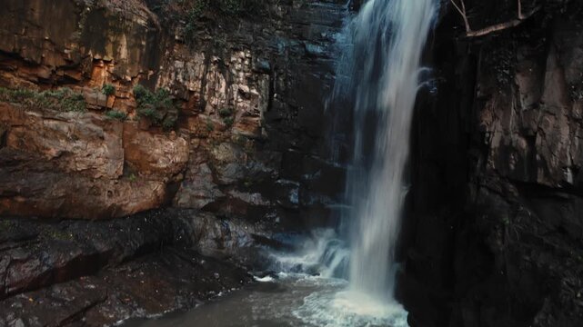 Rugged rocky pool beneath falling water with swirling currents and clear shallow flow. Aerial drone landscape of cascade in a cliff surrounded by lush green Georgian forest. Natural beauty theme