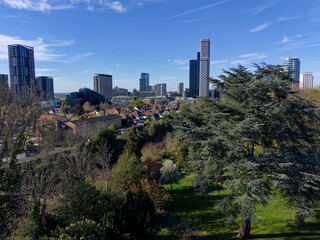 Fototapeta premium Modern Croydon skyline with tall skyscrapers in Greater London. Aerial view towards business district from Park Hill. Green trees with modern architecture in the background. Sunny day with blue sky.
