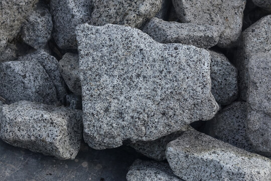 Grey granite stones texture. Close-up pile of rough igneous rock blocks for industrial construction material, coastal riprap, or architectural landscaping background
