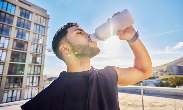 Drinking water, fitness and break with man in city for health, workout rest and mineral hydration. Training recovery, electrolyte drink and wellness with person on rooftop outdoor for detox and h2o