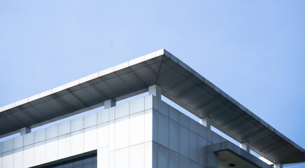 Low angle view of a modern office building exterior with silver metallic cladding and a flat roof structure against a clear blue sky portraying contemporary architecture and corporate real estate © Ari Kusumastuti