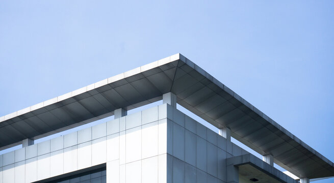Low angle view of a modern office building exterior with silver metallic cladding and a flat roof structure against a clear blue sky portraying contemporary architecture and corporate real estate