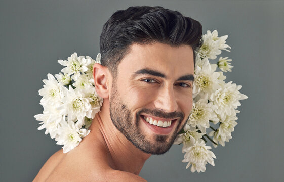 Skincare, flowers and man in studio, natural beauty and portrait with smile on gray background. Person, floral dermatology and organic cosmetics with chrysanthemums, facial treatment or aesthetic