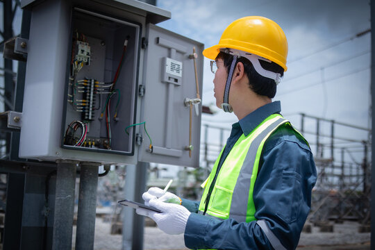 Engineer inspecting an open electrical cabinet at a substation, checking wiring and control components for maintenance, diagnostics, safety compliance, and grid reliability.