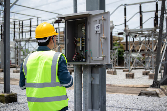 Engineer inspects an open outdoor electrical cabinet at a substation, checking wiring and control components for maintenance, safety, diagnostics, and grid reliability.