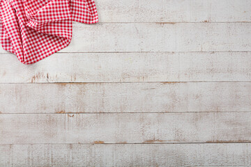White rustic wooden background with folded red checkered napkin in corner. Light colored empty wood planks top view with copy space.