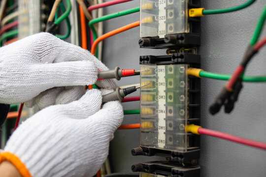 Gloved technician tests terminal wiring with probes inside an electrical control cabinet, supporting diagnostics, maintenance, safety checks, and grid reliability.