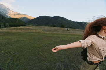 Fototapeta premium Woman in casual beige shirt enjoys expansive outdoors, arms spread, open field with mountain backdrop, conveying freedom and carefree lifestyle moment, under clear sky, warm light, moving wind, sense