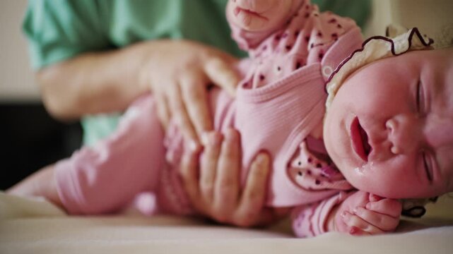 Close up of a baby showing a slight frown or discomfort while being held by an adult