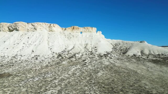 Drone view of low white chalk cliffs, limestone formations, and sparse vegetation in the Mangystau desert. Wild nature, Martian landscapes, unique geology of Kazakhstan, arid climate, weathered rock t