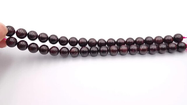 Deep red garnet crystal beads are held and showcased on a vibrant pink thread, highlighting their smooth glossy surface and rich natural color tones perfect for custom artisan jewelry making