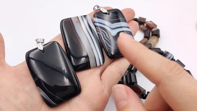 Three large rectangular banded agate gemstone pendants are displayed in an open hand, highlighting their striking black and white striped patterns and smooth polished surface texture