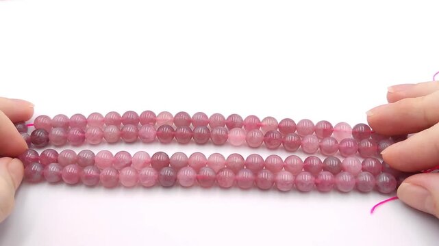 Smooth semi translucent pink strawberry quartz beads are held on a bright cord over a white background, displaying their beautiful natural mineral inclusions for elegant artisan jewelry crafts
