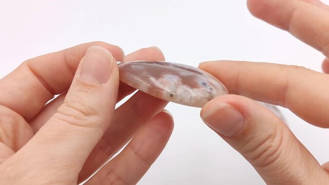 Polished cherry blossom agate pendants in a teardrop shape are held and turned to reveal intricate translucent white and pink floral patterns for custom handmade artisan crystal jewelry designs
