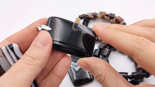 A large rectangular black agate gemstone pendant featuring unique white banded accents and a polished glossy surface is carefully inspected in hand for jewelry craft making supplies