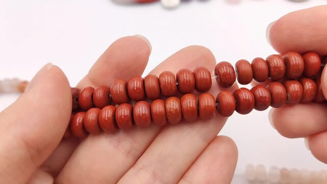 Two strands of polished terracotta red jasper stone beads in a flat abacus rondelle shape are held in an open hand, showcasing their smooth glossy finish and natural microcrystalline texture