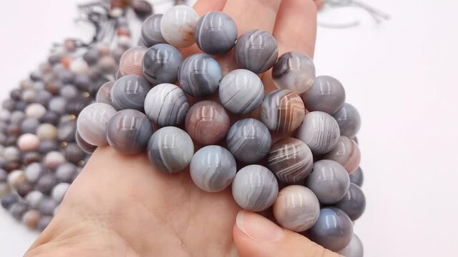 Smooth grey and white striped agate beads are gathered in a hand, showcasing unique circular mineral patterns perfect for crafting handmade artisan jewelry