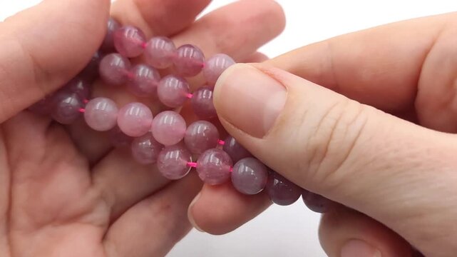 Hands gently separate and hold several strands of smooth, polished pink strawberry quartz gemstone beads strung together on a matching pink cord, displaying their semi-translucent, natural crystalline