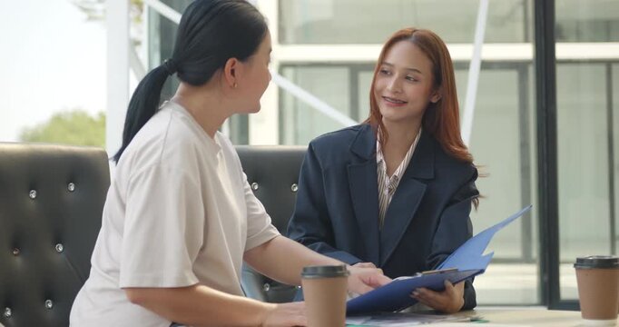 Young Asian businesswoman presenting financial or insurance documents to a mature female client at an outdoor cafe.