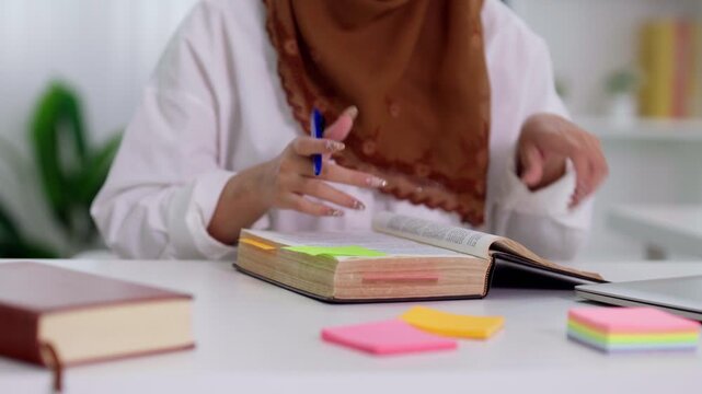 Muslim businesswoman student reading book highlighting notes with marker pen studying research learning for exam at desk workspace with notebook office
