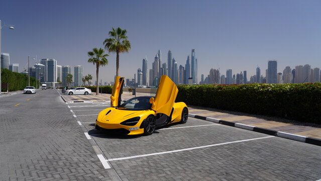McLaren 720S Supercar with Dihedral Doors Open in Papaya Yellow Against Dubai Skyline