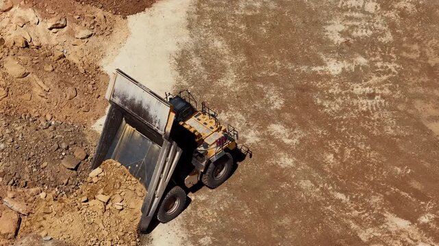 Aerial close up of tractor dumping dirt in mining pit in high desert area
