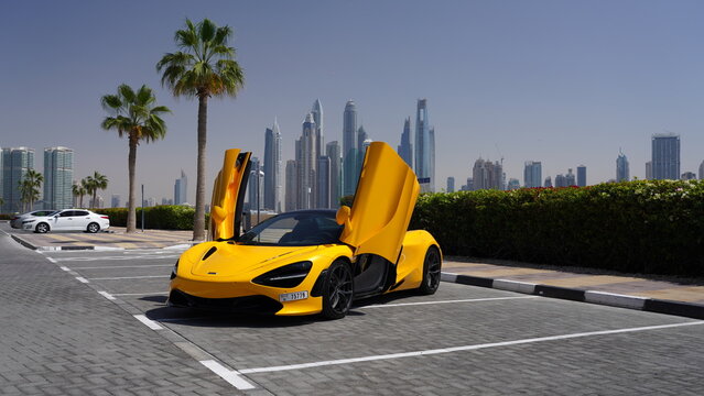 McLaren 720S Supercar with Dihedral Doors Open in Papaya Yellow Against Dubai Skyline