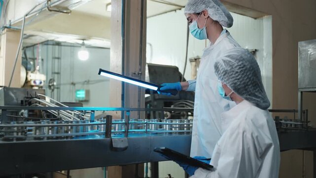 Two female industrial engineers inspect and examine quality control, production process at automate conveyor in canned food manufacturing factory, clean and protective uniforms for hygiene operations.