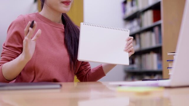 Asian female student teacher holding blank notebook showing empty notepad present ideas content study plan education learning research library bookshelf