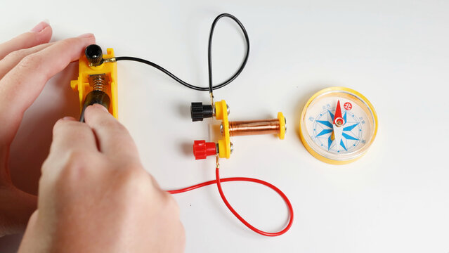 Hands Conducting a Physics Experiment with an Electromagnet and Compass
