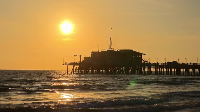 Santa Monica Pier silhouette over Pacific Ocean at sunset, shimmering water with golden reflections and calm coastal evening atmosphere