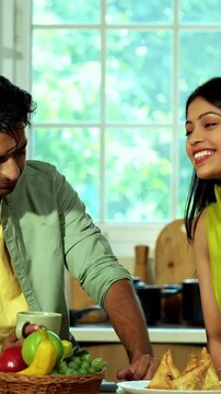 Indian asian young husband and wife having coffee in modern kitchen platform with light hearted chit chat enjoying their morning beverage and talking together in a relaxed home environment