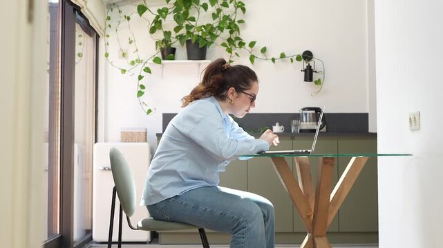 Bored disinterested plus size woman using laptop at home. Bad posture of young female remote working with computer. Tired freelancer unhealthy sitting at table looking for screen. Sedentary lifestyle.