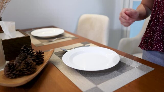 Asian Woman Setting a Dining Table with White Plates and Silverware