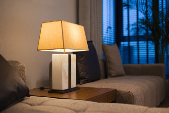 A moody, modern living room featuring a marble-based table lamp that casts a warm glow over a grey tufted sofa and dark accent pillows.