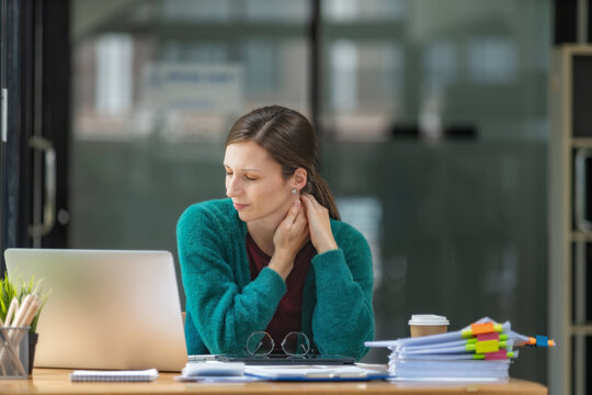 Young businesswoman rubbing her neck feeling pain and stiffness from office syndrome while working on laptop.