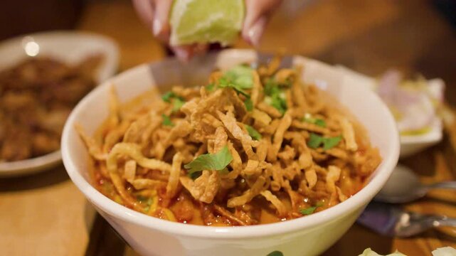 Person Squeezing Fresh Lime Over Northern Thai Khao Soi Curry Noodles