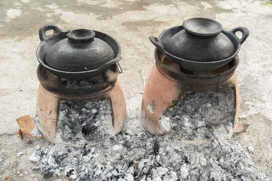 Two traditional Javanese clay stoves with earthenware pots and wood ash on the ground.