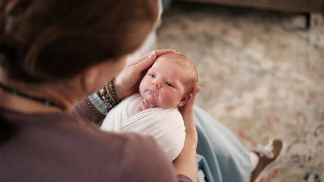 Mom Holds Newborn Baby In Warm Indoor Setting.